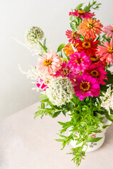 Summer bouquet of colorful Zinnia, onion inflorescences and mint sprigs, bouquet of flowers on the table near the wall, home decoration with flowers