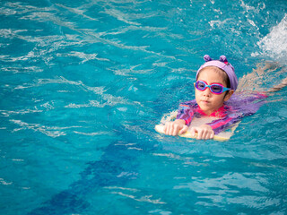 Asian child or kid girl wearing swimming suit to learning on swimming pool , learn and training swim on kick board