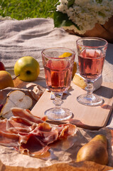 picnic with rose wine, fruits, cheese and prosciutto, close up view of food lying on a plaid
