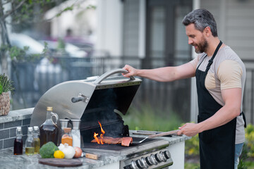 Handsome male preparing barbecue, grill outdoors. Man cooking meat and fish on barbecue in the...