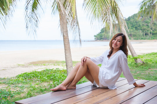 Portrait image of a beautiful young asian woman sitting on wooden balcony by the sea