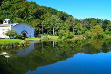 Obraz premium Reflection in the water of jugendstil wasserkraftwerk in Heimbach, Eifel, Germany - surrounded by lush green foliage and blue sky