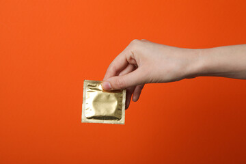 Sealed condom in hand on orange background