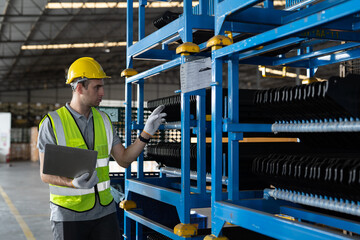 Male warehouse worker wearing safety uniform working with laptop computer and inspecting quality for auto spare parts on shelves for packaging in packaging department at warehouse storage