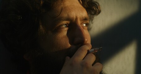 Obraz premium Depressed prisoner in orange uniform sits in prison cell, smokes cigarette. Criminal, inmate serves imprisonment term for crime in jail. Detention center or correctional facility. Close up. Portrait.