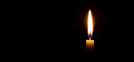Single burning candle flame or light glowing on a small white candle on black or dark background on table in church for Christmas, funeral or memorial service with copy space. - obrazy, fototapety, plakaty