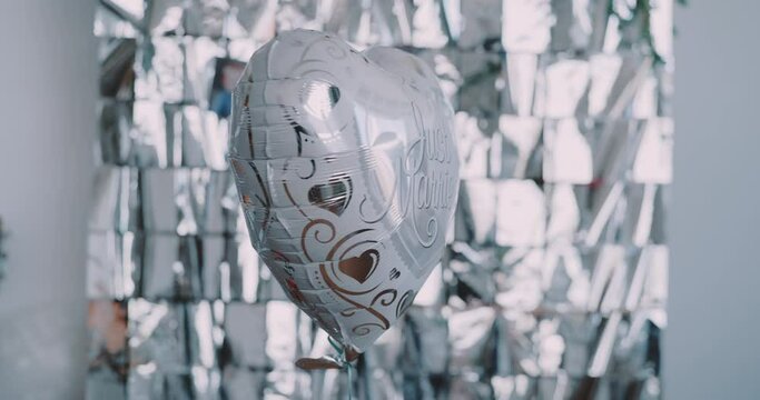 Silver heart shaped balloon with a just married message turning around in a festive background 