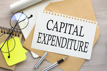 wood background the word CAPITAL EXPENDITURE a torn page on an envelope