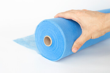 A hand unwinds a roll of blue fabric, a sheet for massage, on a white background.