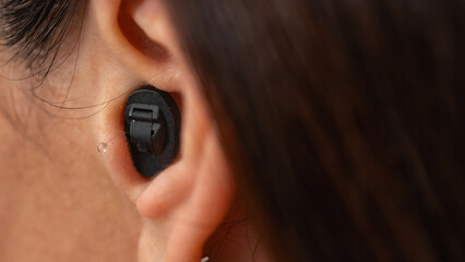 Young woman with a hearing aid hidden in her ear on a light background 