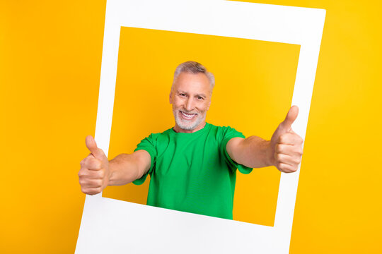 Photo of handsome positive man demonstrate thumb up through paper album card window isolated on yellow color background