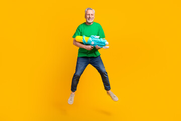 Fototapeta na wymiar Full body portrait of carefree excited aged man jumping arms hold water gun have good mood isolated on yellow color background