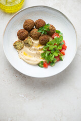 Plate with falafel, hummus, fresh vegetables and greens, top view on a light-beige stone background, vertical shot with space