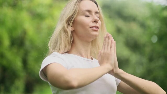 Relaxed young blond woman meditate and breathe slowly while make yoga asanas at park Calm inspired female with closed eyes take break while resting for peaceful mind alone outdoors