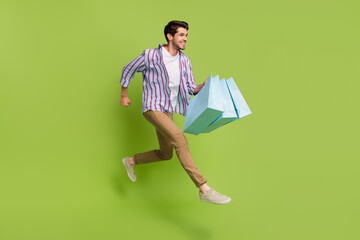 Photo of handsome nice man dressed striped shirt brown trousers run shopping with bags empty space isolated on green color background