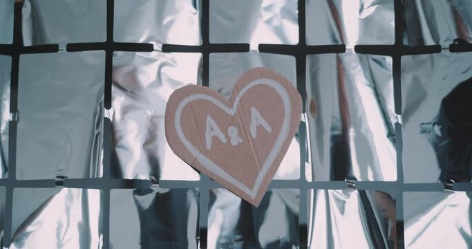 Heart with initials written over a silver background. 