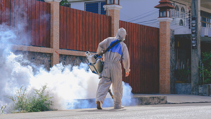 Rear view of healthcare worker in protective clothing using fogging machine spraying chemical to...
