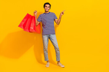 Fototapeta premium Full body portrait of positive nice man hold store bags indicate finger empty space isolated on yellow color background