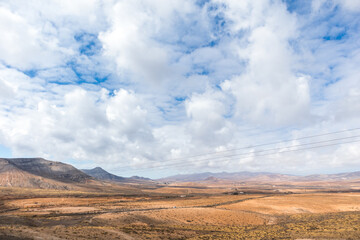 Fototapeta premium Desertic landscape of the interior of Fuerteventura island. Rocky hills with white sand. Sky with big white clouds. Sunny day Fuerteventura, Canary Islands, Spain.