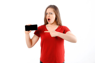Amazed girl show smartphone, looks impressed, pointing index finger blank mobile phone screen, stands over white background