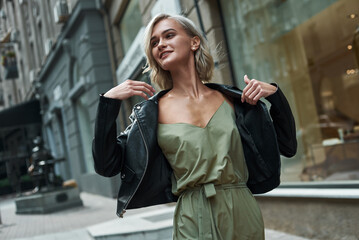 Fashion. Young stylish woman walking on the city street taking off jeans jacket smiling joyful close-up