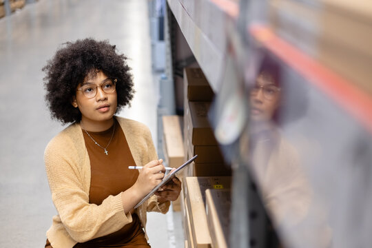 Young African American female looking at camera working in warehouse using digital tablet checking inspection on shelves.woman worker check stock inspecting in storage logistic factory. - Powered by Adobe