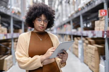 Young African American female looking at camera working in warehouse using digital tablet checking inspection on shelves.woman worker check stock inspecting in storage logistic factory.