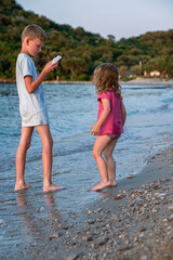 Brother and sister are playing on the beach. A girl and a boy are playing with homemade boats in sea water. Children splash in the Adriatic Sea.