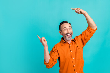 Photo of impressed funky guy wear orange shirt showing two fingers empty space isolated teal color background