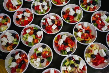 Greek salad in plates of fresh juicy vegetables, feta cheese, herbs and olives in a white bowl on a gray background. Healthy food. Horizontal orientation, top view. Copy space