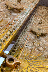 Huge door ajar with islamic andalusian 3D engravings and sculptures in Sidi Boumediene mosque of Tlemcen city in Algeria. A low angle view with metallic latch and handle and feature geometric patterns