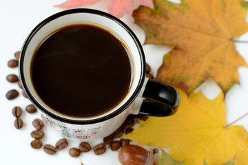 A mug of hot black coffee with steam, dry fallen maple leaves, grains and acorn during golden...
