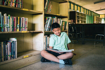 At the library, a young boy of Asian descent is deeply engrossed in reading a book during his break.