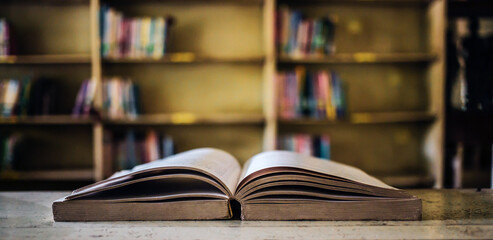 On a wooden table, there's an open book with a library visible in the background. A stack of books nearby adds to the theme of educational learning.