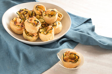 Rolled puff pastry muffins with zucchini slices, vegetarian finger food snack in a white bowl on a...