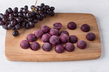 Frozen shaped grape puree on a wooden board with bunch of fresh grapes on a light gray background. Healthy homemade preparations