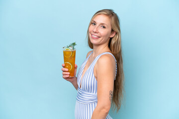 Young blonde woman wearing swimsuit holding a cocktail isolated on blue background smiling a lot