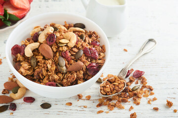 Homemade granola in glass jar with greek yogurt or milk and cashews, almonds, pumpkin with dried cranberry seeds in on white rustic wooden table background. Healthy energy breakfast or snack. Top view
