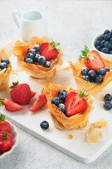 Phyllo or filo pies with fresh berries strawberries and blueberries, cheese filling topped with fresh mint on white plate. Homemade Filo pastry paskets. Delicious filo pastry dessert.