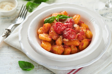 Potato gnocchi. Traditional homemade potato gnocchi with tomato sauce, basil and parmesan cheese on kitchen table on light grey kitchen table background. Traditional Italian food. Top view.