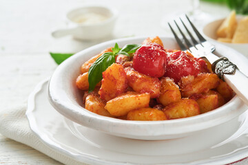 Potato gnocchi. Traditional homemade potato gnocchi with tomato sauce, basil and parmesan cheese on kitchen table on light grey kitchen table background. Traditional Italian food. Top view.
