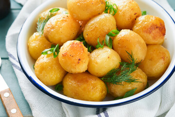 Fresh boiled new or young potatoes with butter, fresh dill and onions in white bowl on old rustic wooden background. Tasty new boiled potatoes. Top view.