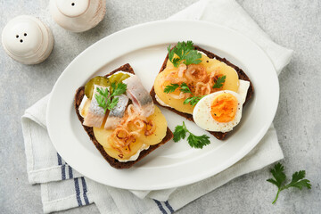 Open sandwich or smorrebrod with rye bread, herring, eggs, caramelized onions, parsley and cottage cheese on old wooden rustic table backgrounds. Danish or Scandinavian traditional food snack lunch.