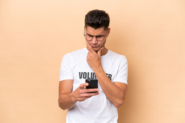 Young volunteer caucasian man isolated on beige background thinking and sending a message