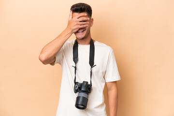 Young photographer caucasian man isolated on beige background covering eyes by hands and smiling
