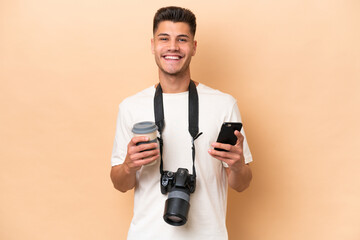 Fototapeta na wymiar Young photographer caucasian man isolated on beige background holding coffee to take away and a mobile