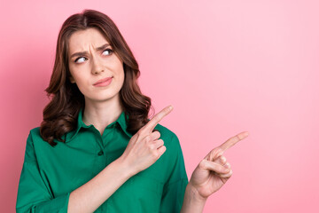 Photo of pretty doubtful lady wear green shirt pointing two fingers looking empty space isolated pink color background