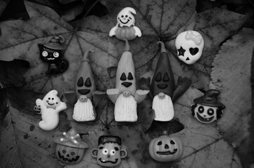 Funny figures of Halloween-themed characters. Gnomes, ghost, cat, pumpkin. Toys on the background of autumn leaves. Black and white photo.