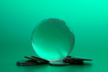 A glass globe with coins on a green background. Financial symbol.