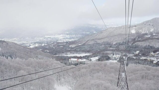 Point of view cableway moving up to snowy mountain peak ski resort. Aerial view of pine tree forest mountain covered in snow under cable car. Ski lift transportation and winter travel vacation concept